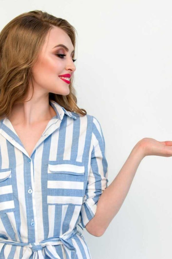 Stylish woman gazing sideways with open palm in a blue striped dress against a white wall.