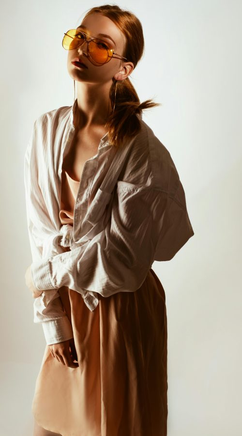 Trendy woman posing in oversized shirt and sunglasses, exuding modern fashion style.