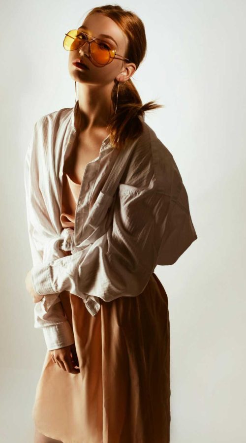 Trendy woman posing in oversized shirt and sunglasses, exuding modern fashion style.