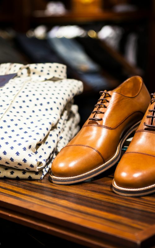Elegant brown leather shoes and printed shirt displayed on a wooden table in a stylish clothing store.