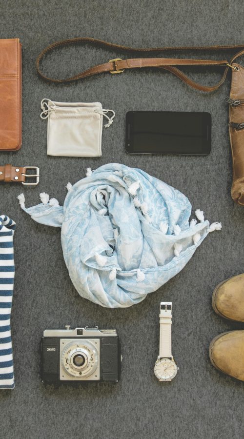 Vintage travel essentials flat lay with leather bags, shoes, camera, and clothing.