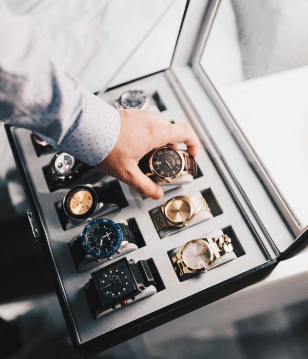 A sophisticated display of luxury watches in an elegant case with a hand selecting one.