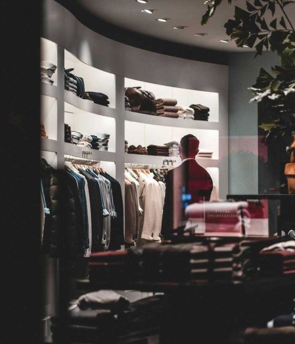 Back view of faceless elegant male customer in suit choosing new clothes while standing near wardrobe in modern fashion boutique