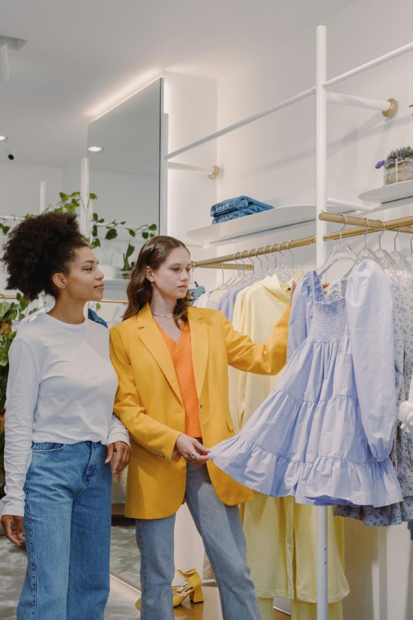 Two women explore a variety of stylish dresses on a clothing rack inside a chic fashion store.