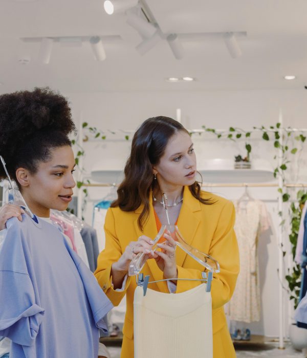 Two women shopping for trendy clothes in a stylish boutique with plant decor.