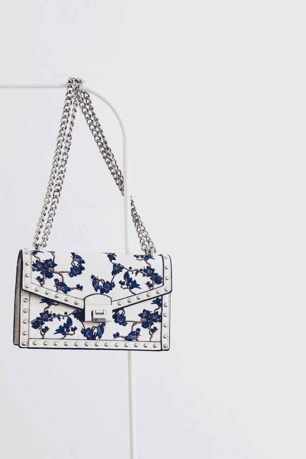 Elegant white handbag with blue floral design and silver chain, perfect for fashion enthusiasts.