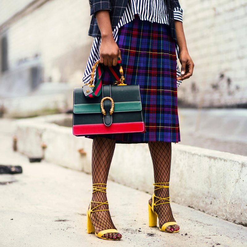 Fashion-forward outfit with plaid skirt and colorful handbag in urban setting.