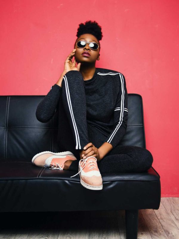 Fashionable woman posing confidently on a sofa in a modern studio setting.